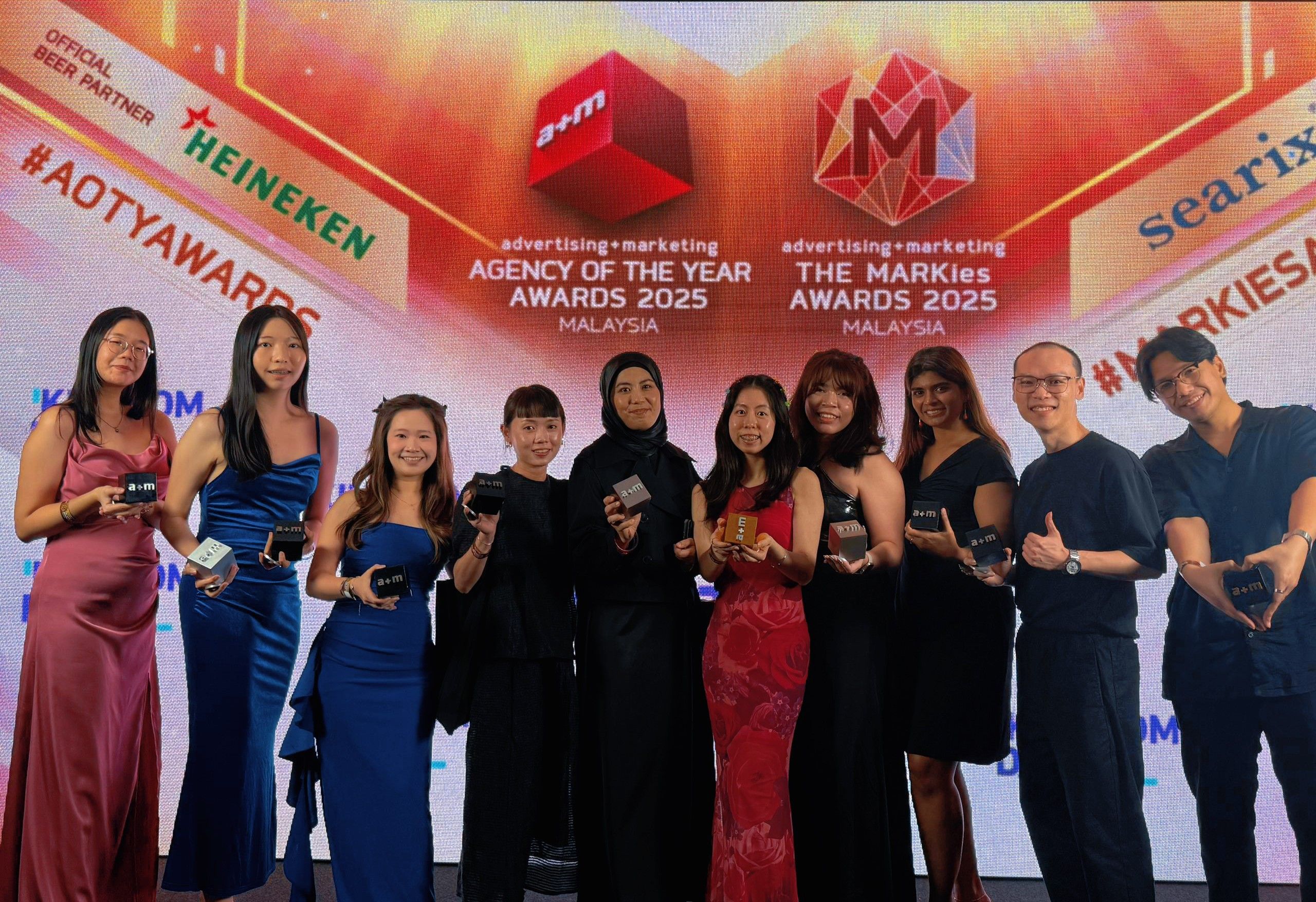 Kingdom Digital heroes smiling in formal attire holds awards at the Agency of the Year 2025 event in Malaysia, with a colorful backdrop.